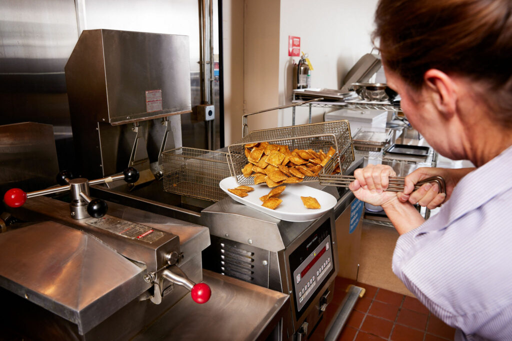 Woman Taking Ravioli Out Of Henny Penny Open Fryer